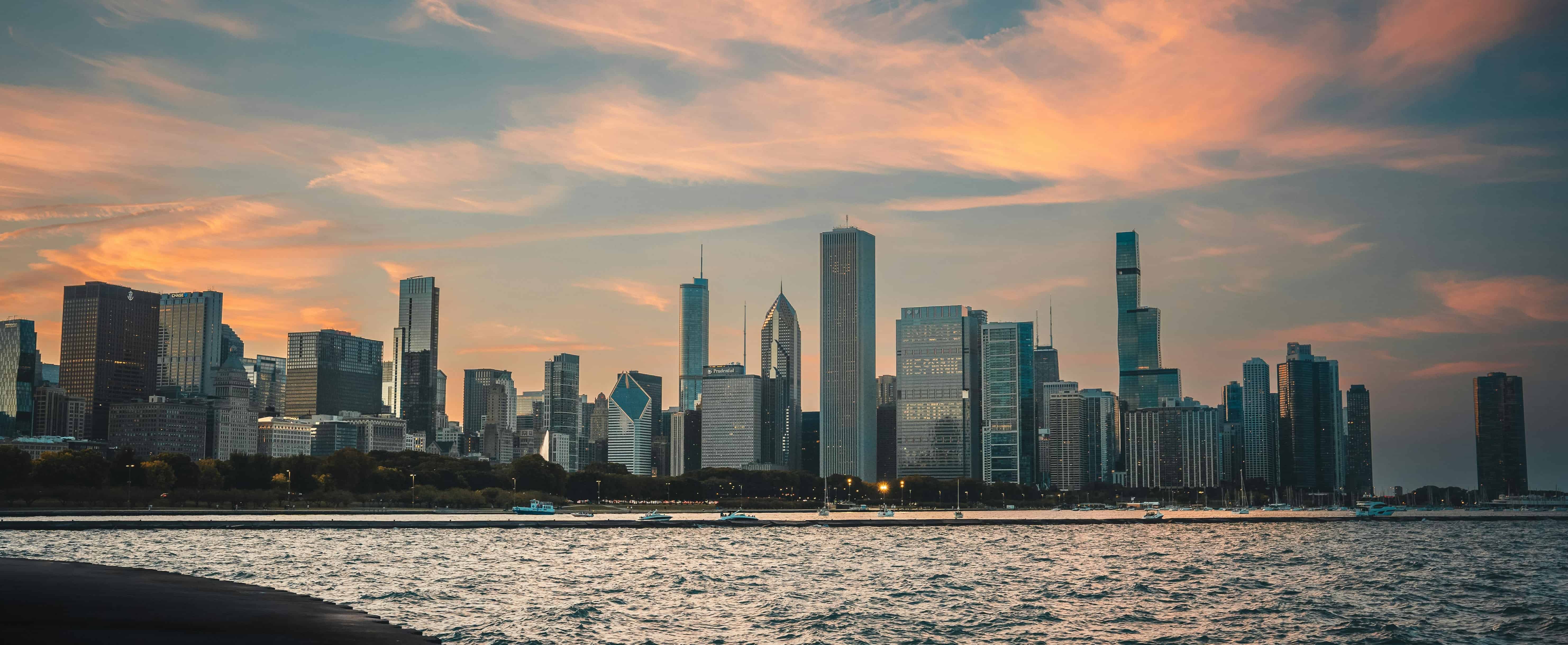 A panoramic view of the Chicago skyline at sunset, reflecting on Lake Michigan.