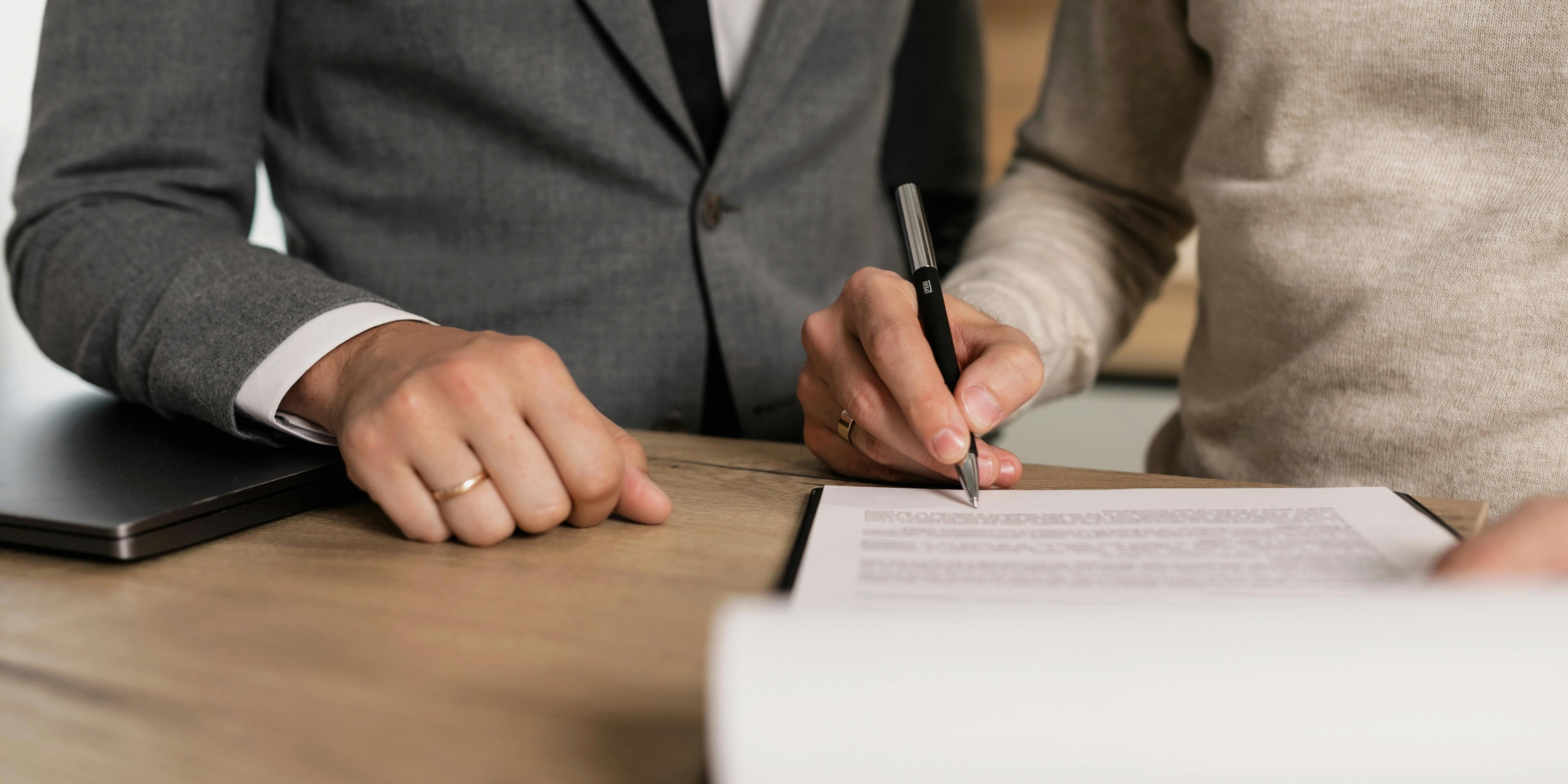 Two people reviewing and signing a document on a wooden desk