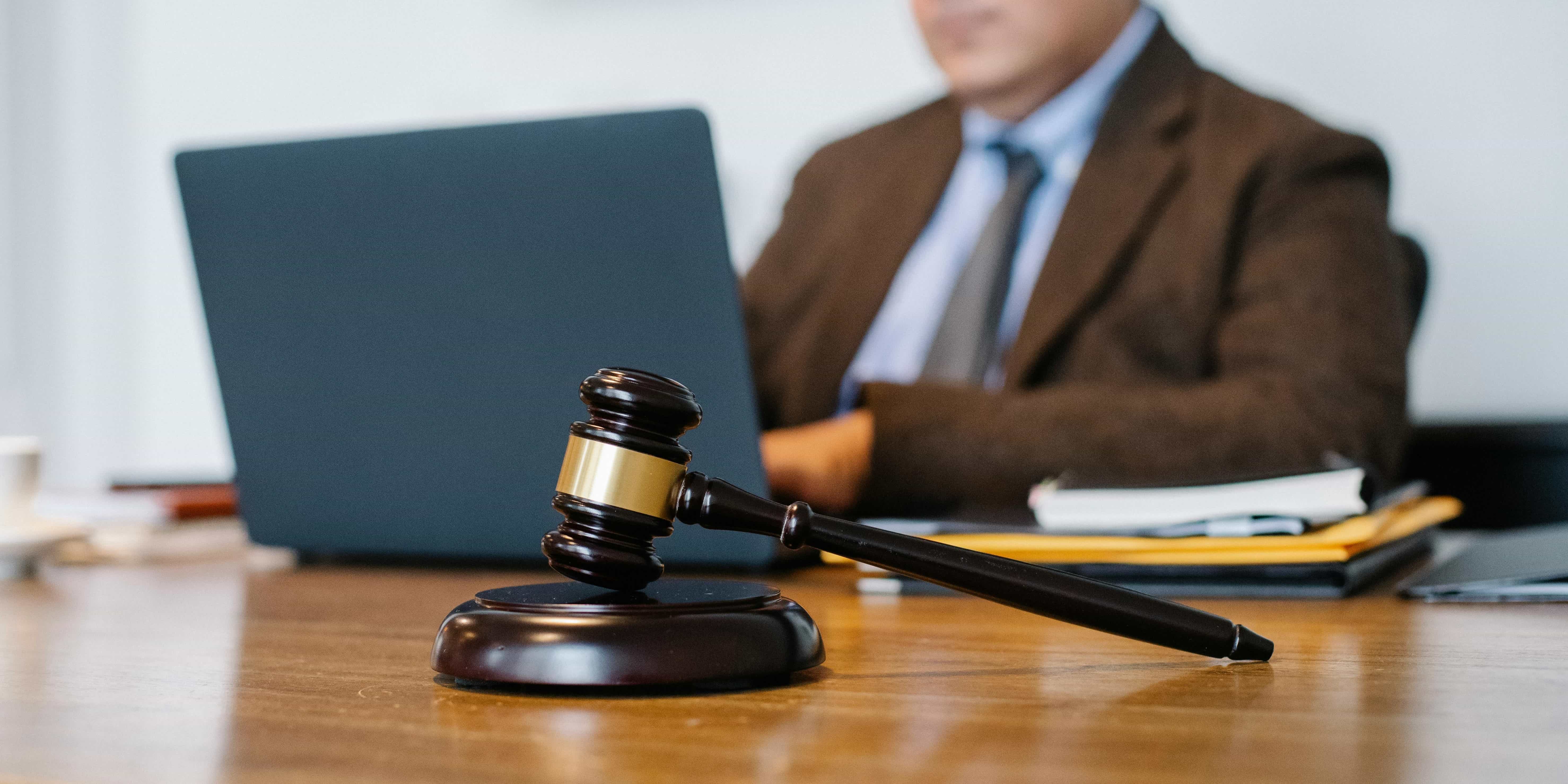 Wooden judge's gavel on a desk with a blurred lawyer working