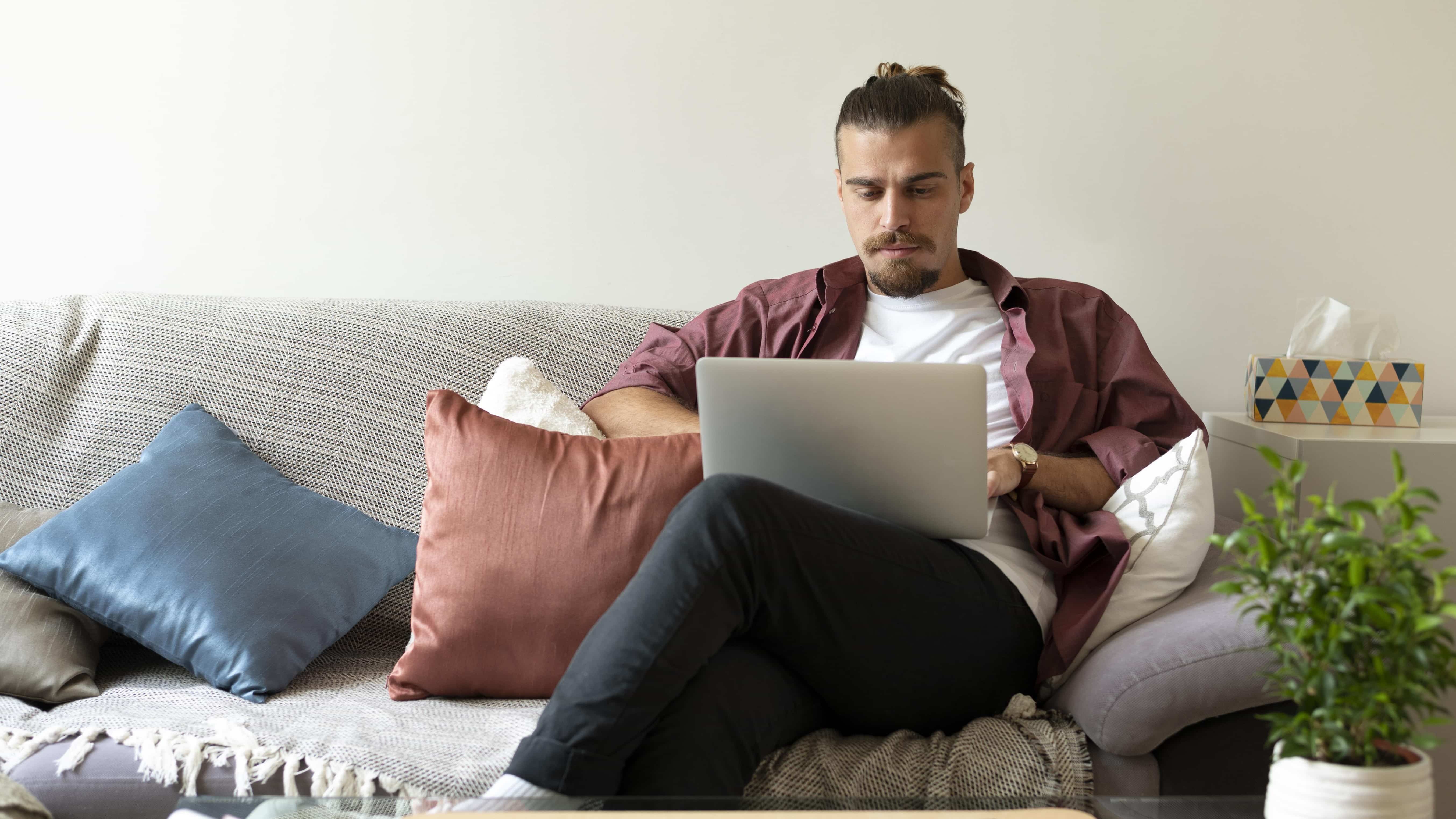 Medium shot man working with laptop on couch