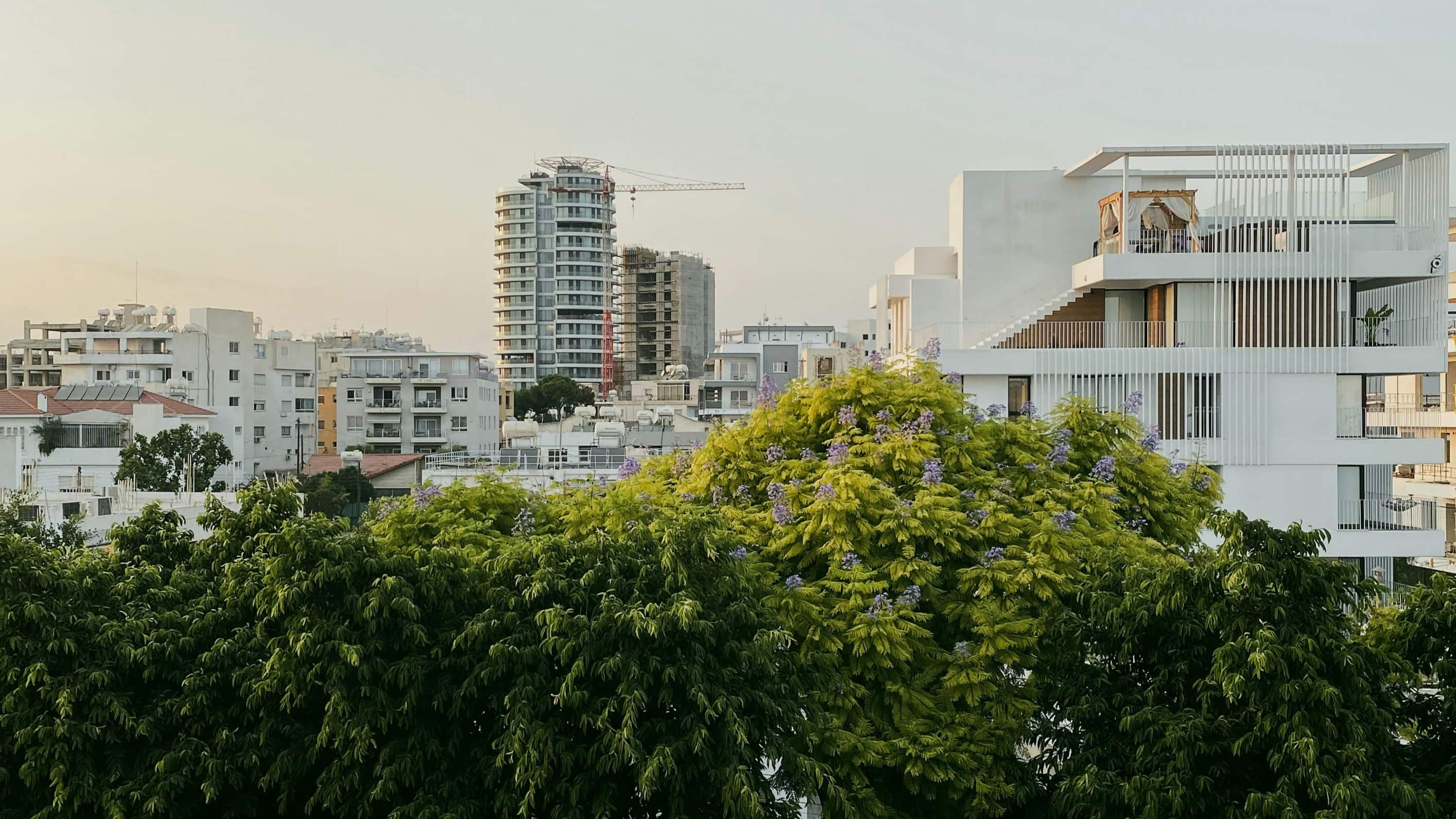 A city skyline with tall buildings and lush greenery in the foreground.