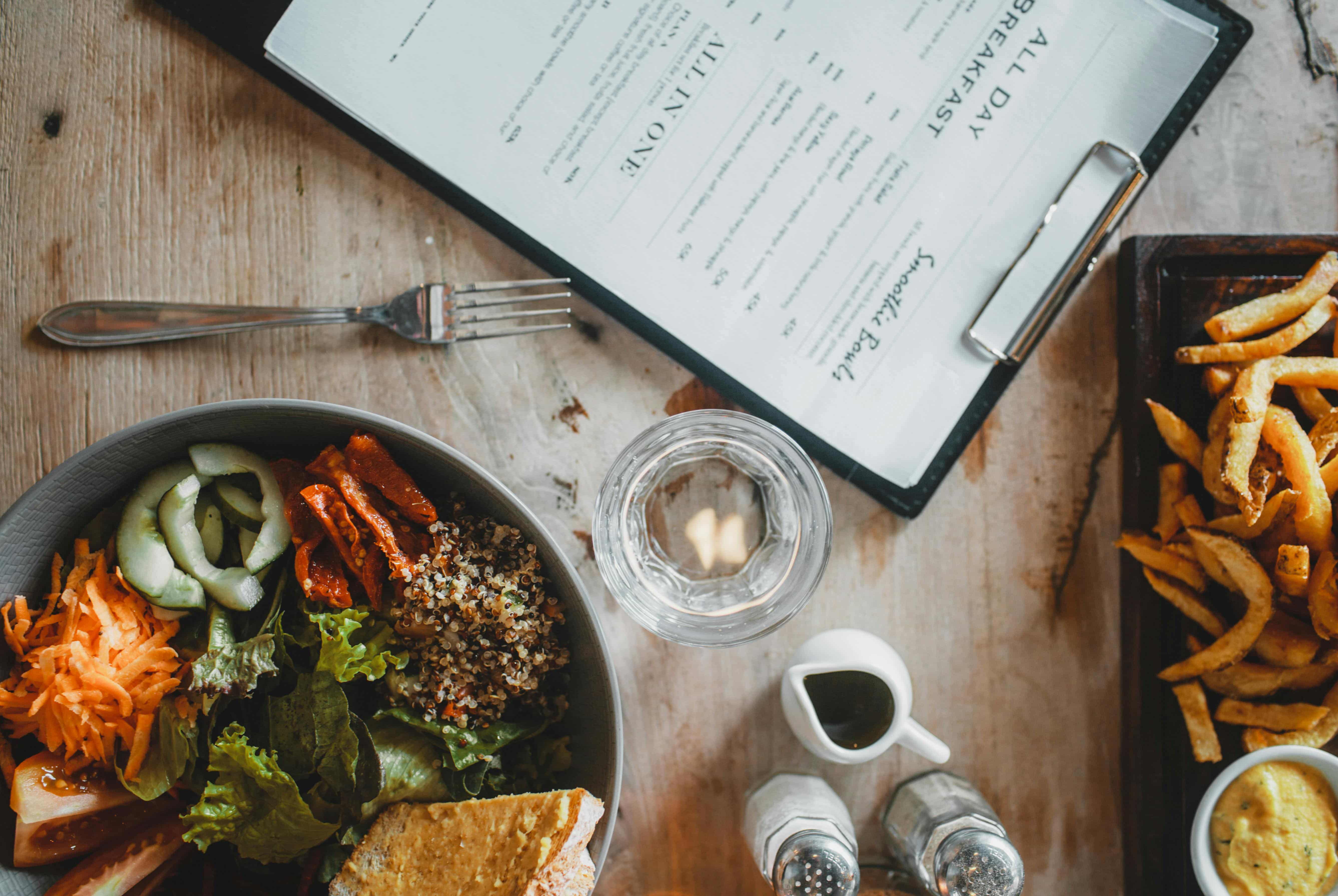 A wooden table with a plate of salad, a glass of water, and a menu