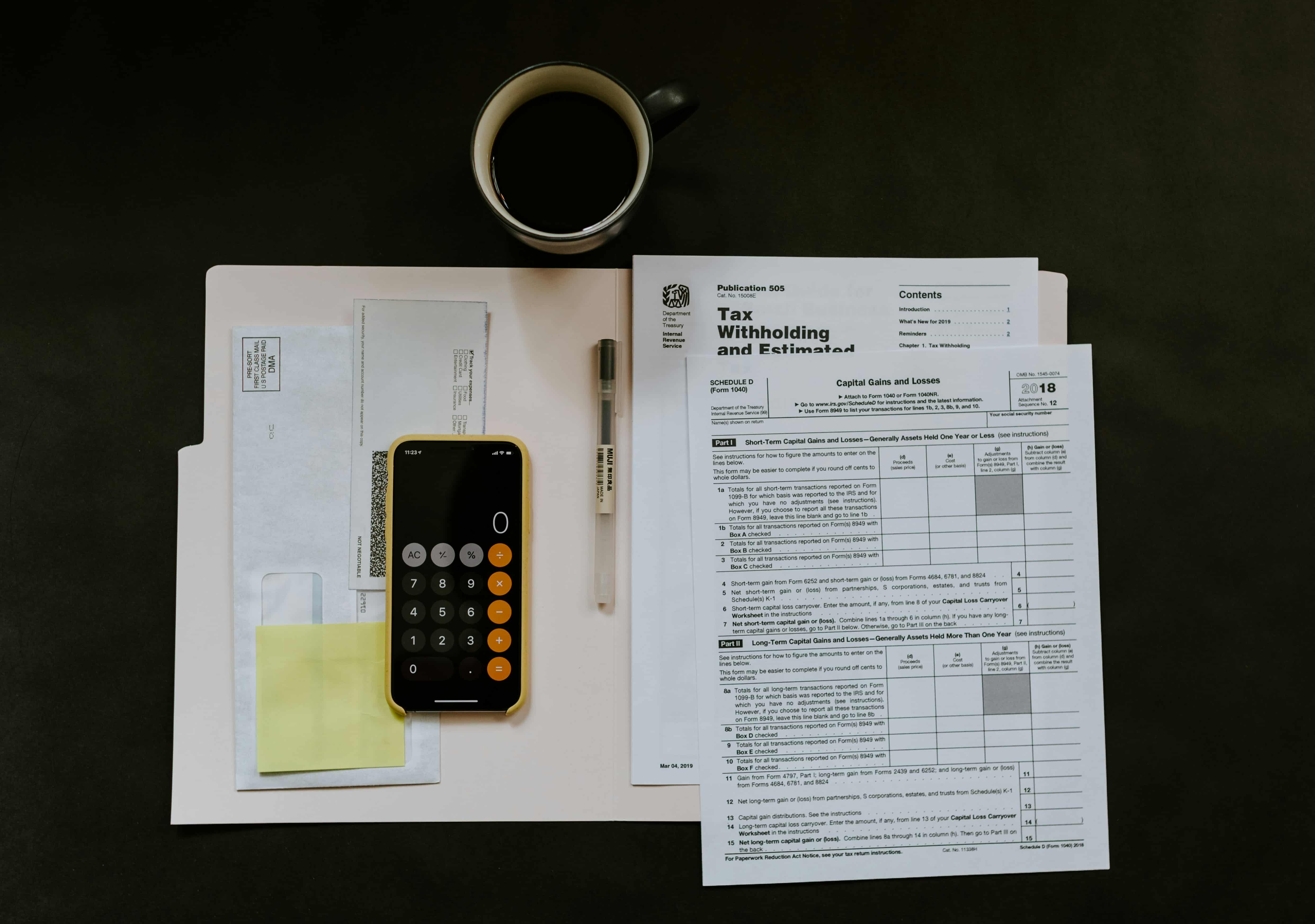 A desk with a cup of coffee, a calculator, a smartphone, a pen, and tax forms.